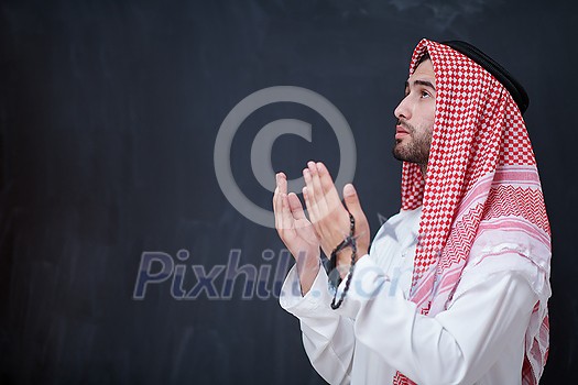 young arabian man in traditional clothes making traditional prayer to God, keeps hands in praying gesture in front of black chalkboard representing modern islam fashion and ramadan kareem concept young arabian man in traditional clothes making traditional prayer to God, keeps hands in praying gesture in front of black chalkboard representing modern islam fashion and ramadan kareem concept