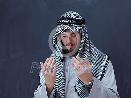 young arabian man in traditional clothes making traditional prayer to God, keeps hands in praying gesture in front of black chalkboard representing modern islam fashion and ramadan kareem concept young arabian man in traditional clothes making traditional prayer to God, keeps hands in praying gesture in front of black chalkboard representing modern islam fashion and ramadan kareem concept