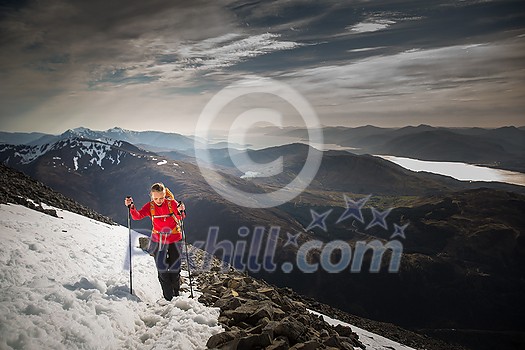 Pretty, young female hiker going uphill with splendid hills around her