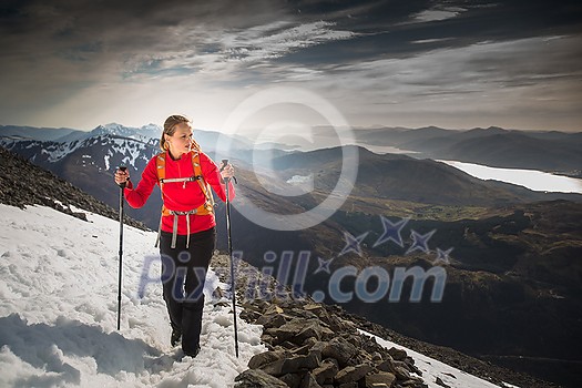 Pretty, young female hiker going uphill with splendid hills around her