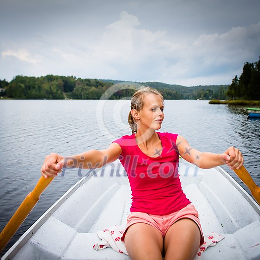 Happy, young woman enjoying rowing boat ride on a lake on a summer day