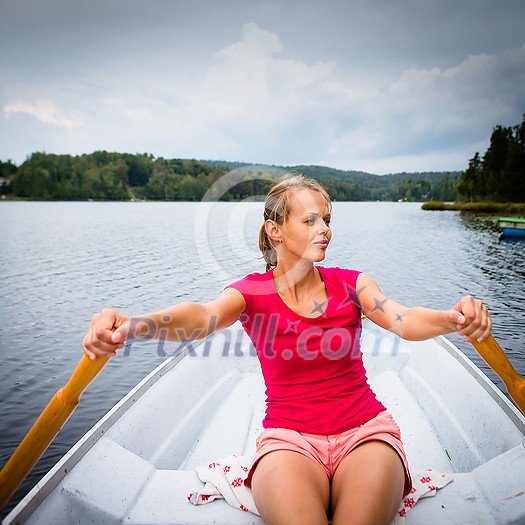 Happy, young woman enjoying rowing boat ride on a lake on a summer day Happy, young woman enjoying rowing boat ride on a lake on a summer day