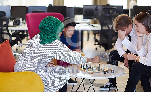 multiethnic group of business people playing chess while having a break in relaxation area at modern startup office