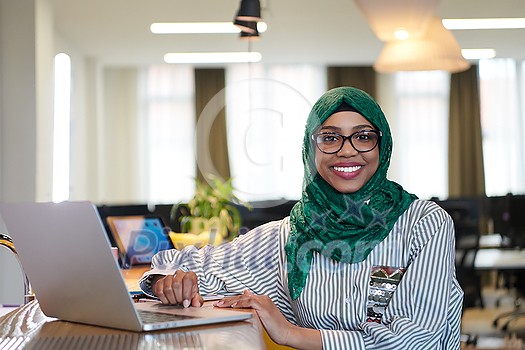 african muslim business woman wearing a green hijab while working on laptop computer in relaxation area at modern open plan startup office. Diversity, multiracial concept