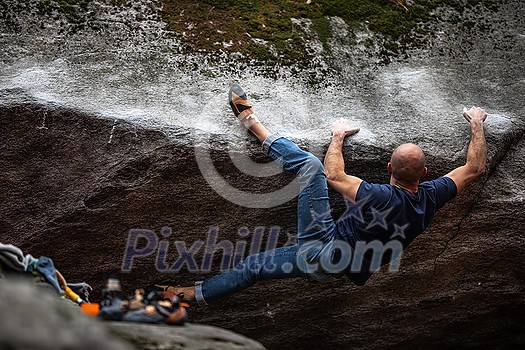 A rock climber climbing on a boulder rock outdoors. Group of friends involved in sports outside.