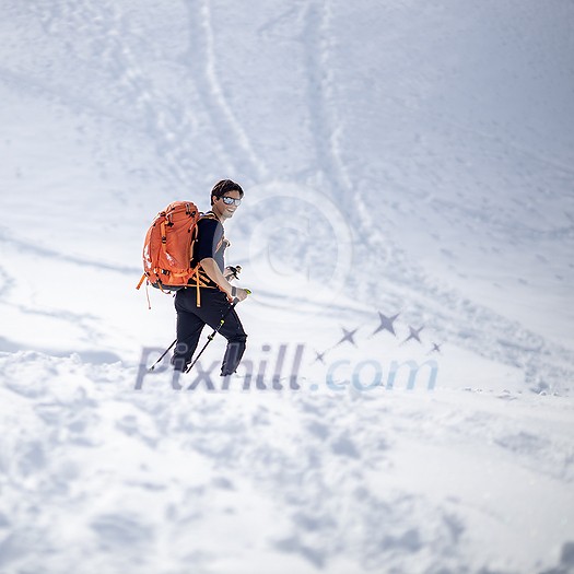 Winter sports - young man walking with snowshoes/touring skis in high mountains covered with lots of snow (selective focus on the mountain in the background)