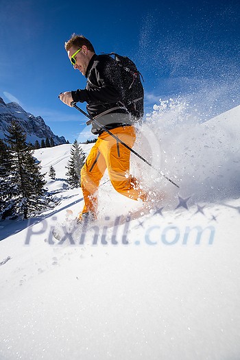 Winter sports - young man running with snowshoes downhill in high mountains covered with lots of snow
