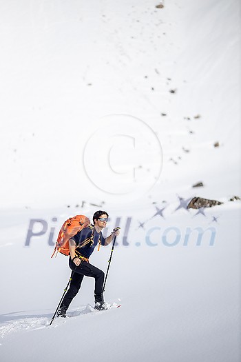 Winter sports - young man walking with snowshoes in high mountains covered with lots of snow (selective focus on the mountain in the background)