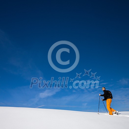 Winter sports - young man walking with snowshoes uphill in high mountains covered with lots of snow (selective focus on the mountain in the background)