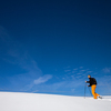 Winter sports - young man walking with snowshoes uphill in high mountains covered with lots of snow (selective focus on the mountain in the background)