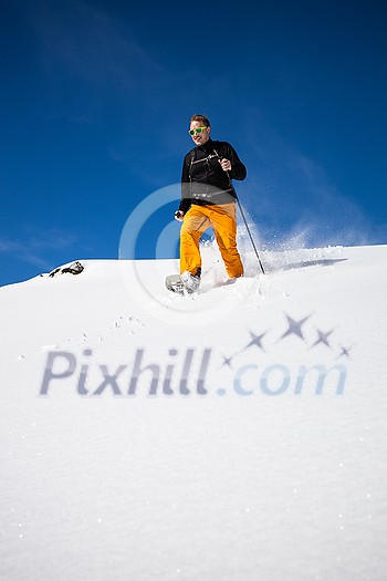 Winter sports - young man running with snowshoes downhill in high mountains covered with lots of snow