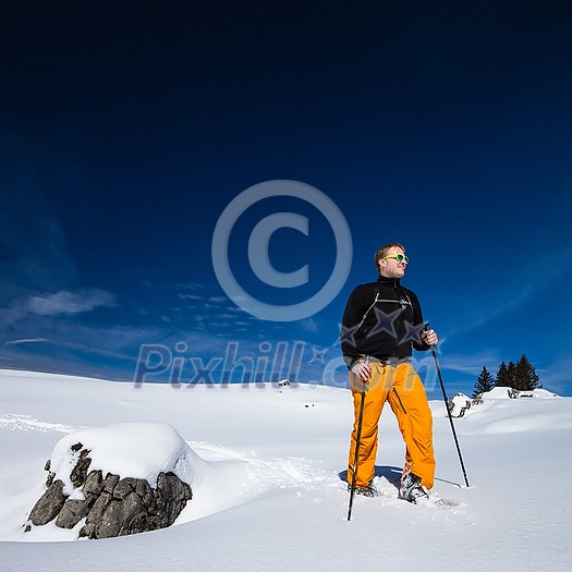 Winter sports - young man walking with snowshoes uphill in high mountains covered with lots of snow (selective focus on the mountain in the background)