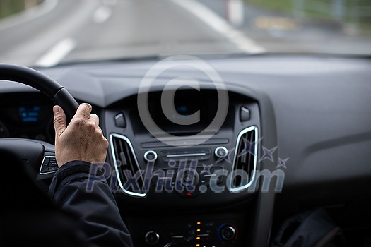 Driver's hands on a steering wheel of a car and blue sky with blurred clouds