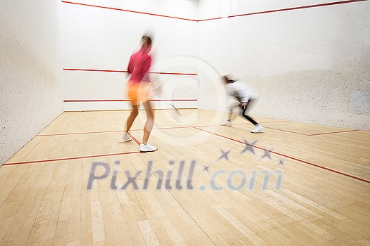 Two female squash players in action on a squash court (motion blurred image; color toned image)