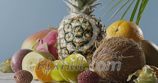 Ripe pineapple with fresh natural exotic fruits on a wooden table on a blue background. Vertical panoramic motion 4K UHD video, 3840, 2160p. Concept of vegetarian diet eating.