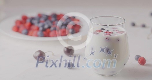 A glass with mix berries and milk. A plate filled raspberries, blueberries, cherries on a white table. The focus changes from the glass to the plate. Shallow depth of field. Slow motion video, 4K.