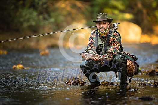 Close-up view of the hands of a fly fisherman holding a lovely trout while  fly fishing on a splendid mountain river