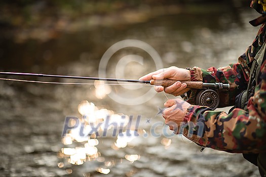 Close-up view of the hands of a fly fisherman working the line and the fishing rod while fly fishing on a splendid mountain river for rainbow trout