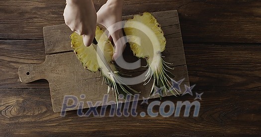 Woman's hands are cutiing the halves of fresh yellow natural tropical pineapple in a quater. Four parts of fruit on a cutting board on a wooden table. Top view. Motion, 4K UHD video, 3840, 2160p.