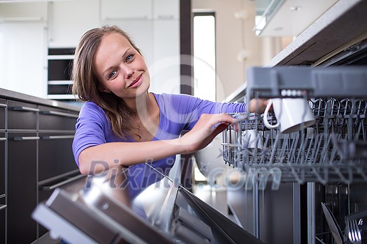 Pretty, young woman in her modern and well equiped kitchen putting cups into the dishwasher - an appliance that helps her keep the home tidy Pretty, young woman in her modern and well equiped kitchen putting cups into the dishwasher - an appliance that helps her keep the home tidy