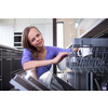 Pretty, young woman in her modern and well equiped kitchen putting cups into the dishwasher - an appliance that helps her keep the home tidy