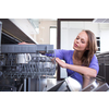 Pretty, young woman in her modern and well equiped kitchen putting cups into the dishwasher - an appliance that helps her keep the home tidy