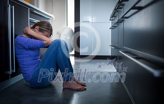 Depressed young woman, sitting on the kitchen floor, feeling down