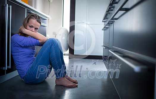 Depressed young woman, sitting on the kitchen floor, feeling down