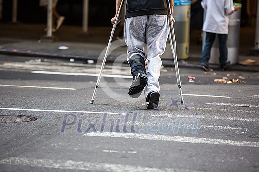 Man with crutches crossing a street