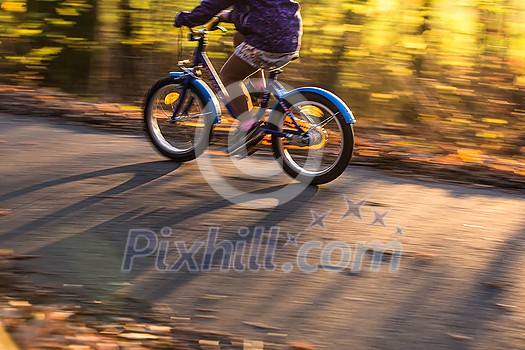 Little boy going fast on his little bike on a forest path in warm evening light