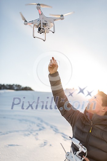 Young man controlling his drone in snowy outdoors. Drone operator holding a transmitter and landing with a drone. Young man controlling his drone in snowy outdoors. Drone operator holding a transmitter and landing with a drone.