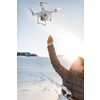 Young man controlling his drone in snowy outdoors. Drone operator holding a transmitter and landing with a drone.