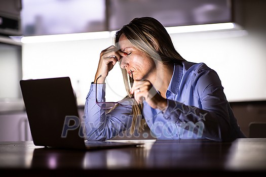 Pretty, middle-aged woman working late in the day on a laptop computer at home, running a business from home/working remotely - getting frustrated