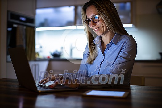 Pretty, middle-aged woman working late in the day on a laptop computer at home, running a business from home
