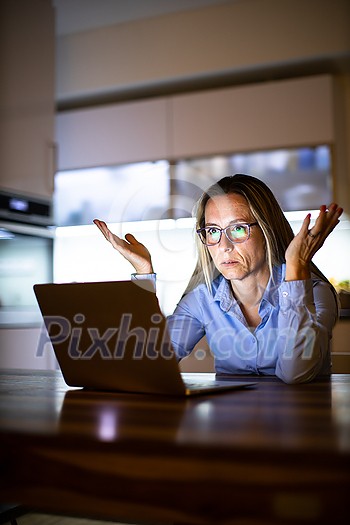 Pretty, middle-aged woman working late in the day on a laptop computer at home, running a business from home/working remotely - getting frustrated
