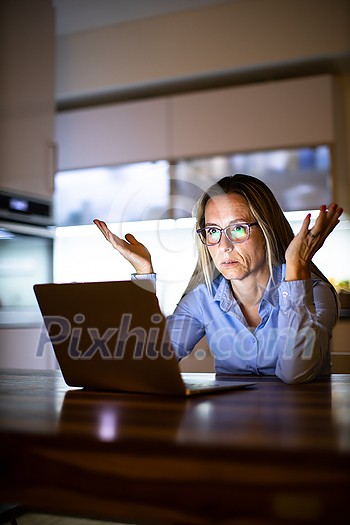 Pretty, middle-aged woman working late in the day on a laptop computer at home, running a business from home/working remotely - getting frustrated Pretty, middle-aged woman working late in the day on a laptop computer at home, running a business from home/working remotely - getting frustrated
