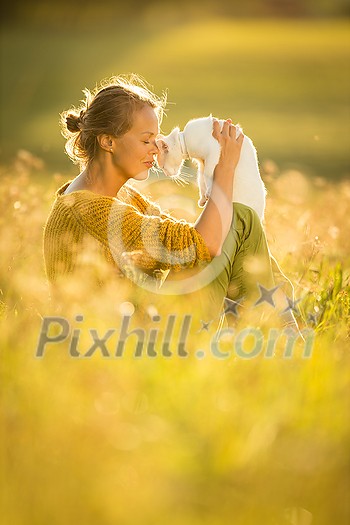 Pretty, young woman with her cat pet sitting in grass on lovely meadow lit by warm evening light (shallow DOF; color toned image)