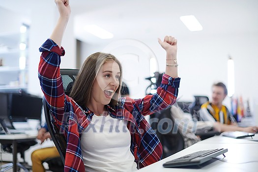 happy casual business woman celebrating success while working on desktop computer in modern open plan startup office interior