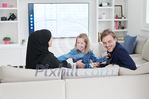 Happy Muslim family with daughter woman in traditional fashionable dress having fun and good time together while sitting on sofa during the month of Ramadan at modern home