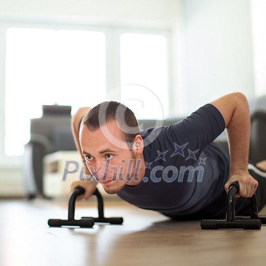 Handsome young man working out at home, using his own bodyweight for exercise, doing push-ups in the living room Handsome young man working out at home, using his own bodyweight for exercise, doing push-ups in the living room