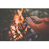 Young woman making fire while camping outdoors, in an alpine wilderness - warming up her hands near the fire