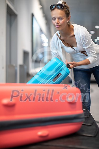 Young woman with her luggage at an international airport, waiting for her luggage to arrive at the baggage claim zone