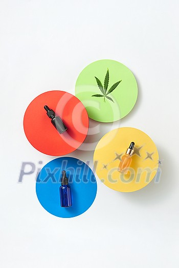 Multicolored paper round cards with bottles of natural medical cannabis essential CBD oil on a light grey background, copy space. Use of cannabis for medical purposes. Top view.