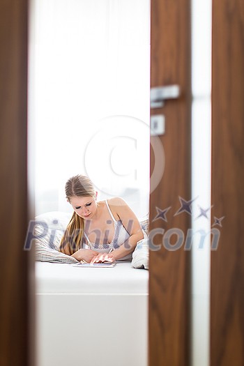 Beautiful young woman in her bed, using a tablet computer in the morning Beautiful young woman in her bed, using a tablet computer in the morning