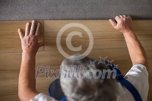 DIY, repair, building and home concept - close up of male hands lying parquet floor board/laminate flooring (shallow DOF; color toned image)