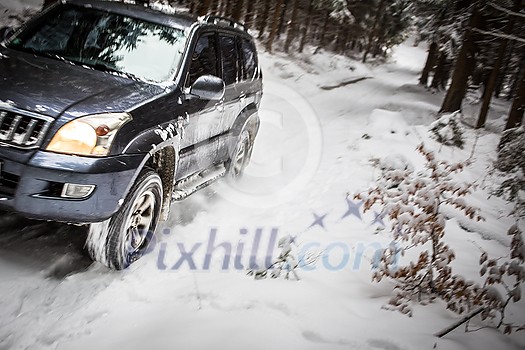 Motion blurred image of a big suv car going fast on a snow covered forest road