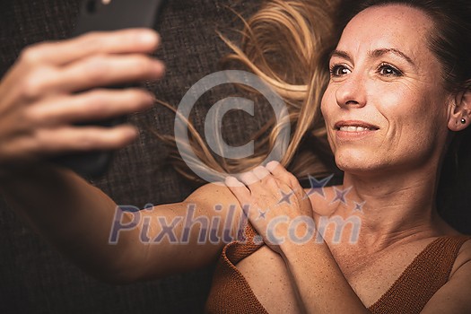 Happy mid-aged woman taking selfie with her smart phone at home Happy mid-aged woman taking selfie with her smart phone at home