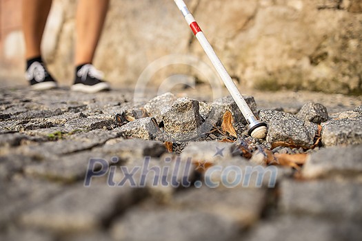 Blind woman walking on city streets, using her white cane to navigate the urban space better and to get to her destination safely Blind woman walking on city streets, using her white cane to navigate the urban space better and to get to her destination safely
