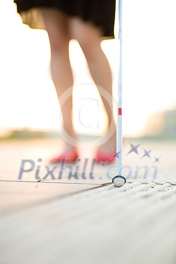 Blind woman walking on city streets, using her white cane to navigate the urban space better and to get to her destination safely Blind woman walking on city streets, using her white cane to navigate the urban space better and to get to her destination safely