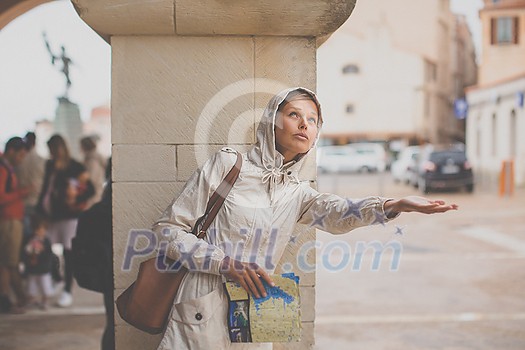 Gorgeous female tourist with a map discovering a foreign city - waiting for the rain to stop (shallow DOF; color toned image)